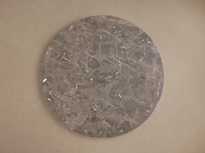 Saint Germain Round Stone Dining Table with marble top and elegant steel Launette base on wooden floor, set against beige wall.