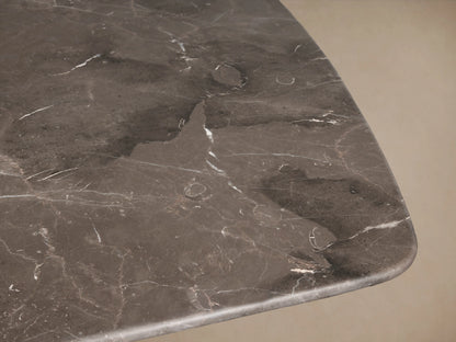 Stone dining table with an espresso brown top showing natural veining, supported by a brass-finished steel base, on a wooden floor.