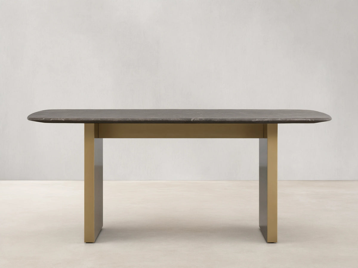 Stone dining table with an espresso brown top showing natural veining, supported by a brass-finished steel base, on a wooden floor.