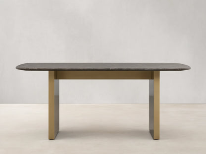 Stone dining table with an espresso brown top showing natural veining, supported by a brass-finished steel base, on a wooden floor.