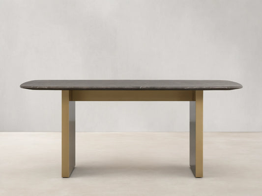 Stone dining table with an espresso brown top showing natural veining, supported by a brass-finished steel base, on a wooden floor.