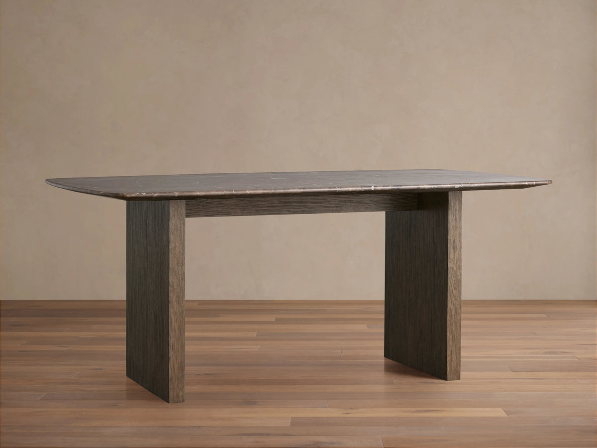 Saint Germain dining table with rectangular stone top and wood base. Dark finish, set on light wood flooring and beige wall.