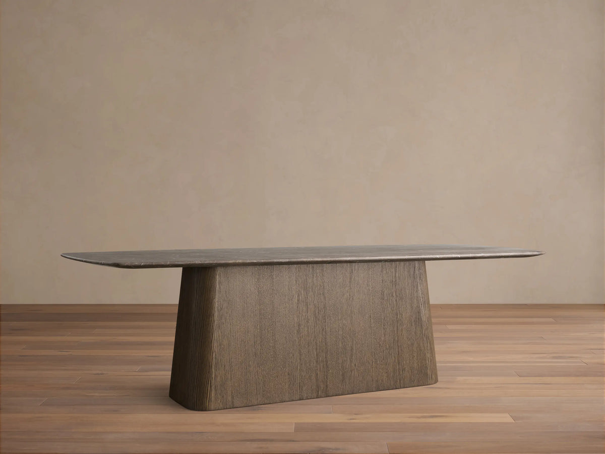 Saint Germain Dining Table. Espresso stone top, rounded corners, dark wood Toulouse base on wood floor against beige wall.