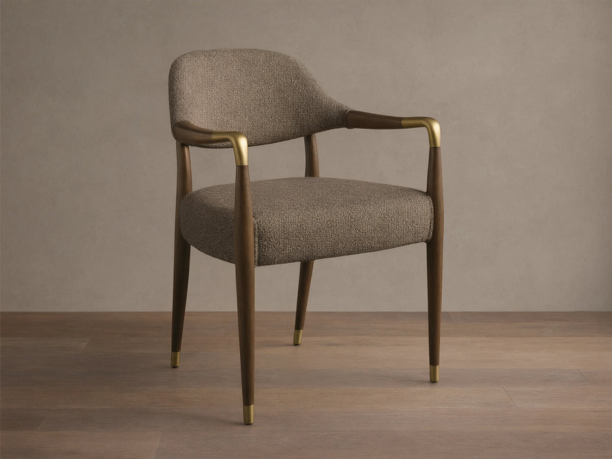 Front view, angled, of the Evelyn Dining Arm Chair with brownish-grey textured upholstery, dark brown mahogany frame, and brushed brass accents.