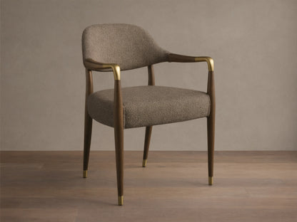 Front view, angled, of the Evelyn Dining Arm Chair with brownish-grey textured upholstery, dark brown mahogany frame, and brushed brass accents.