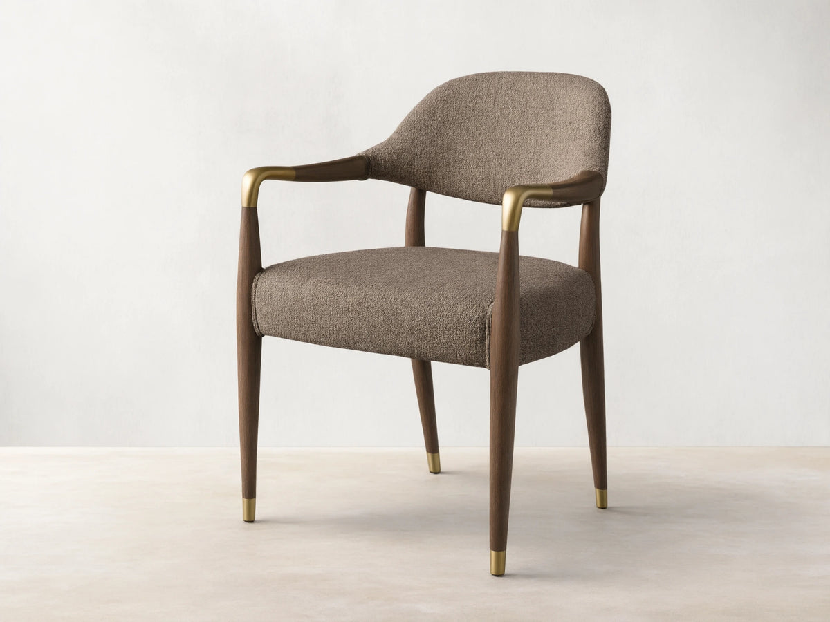 Front view, angled, of the Evelyn Dining Arm Chair with brownish-grey textured upholstery, dark brown mahogany frame, and brushed brass accents.