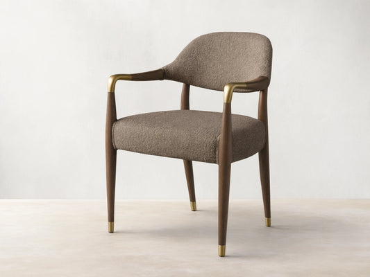 Front view, angled, of the Evelyn Dining Arm Chair with brownish-grey textured upholstery, dark brown mahogany frame, and brushed brass accents.