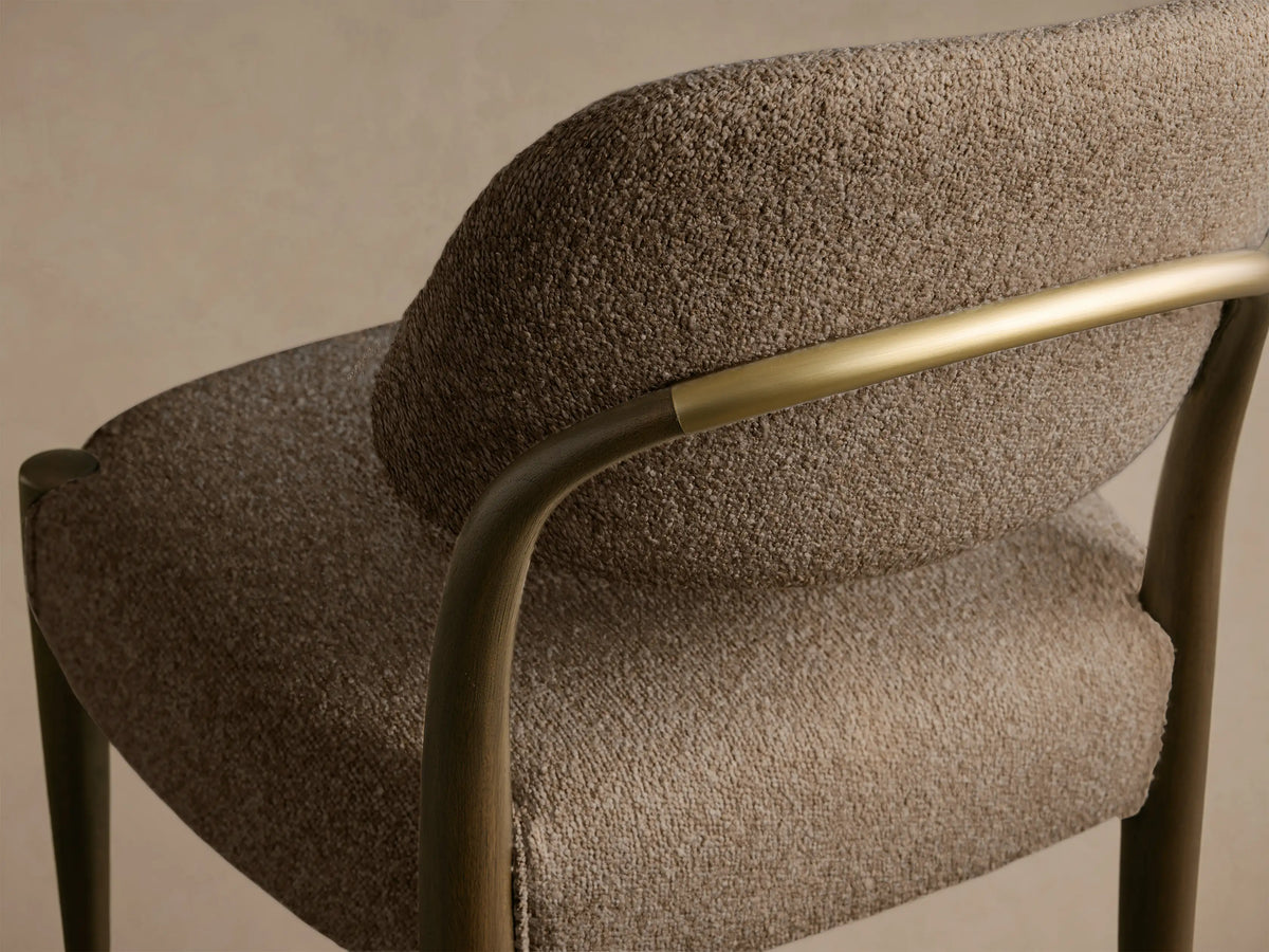 Close-up of the Evelyn Dining Side Chair, showing its textured taupe upholstery, dark mahogany wood frame, and warm brushed brass accent.