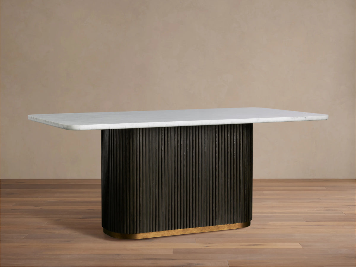 Finnley Dining Table with a smooth white rectangular top and a textured dark base on a wooden floor, against a beige wall.