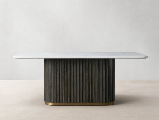 Finnley Dining Table with a white rectangular marble top, dark vertical ribbed base, and light brass plinth on wooden floor.