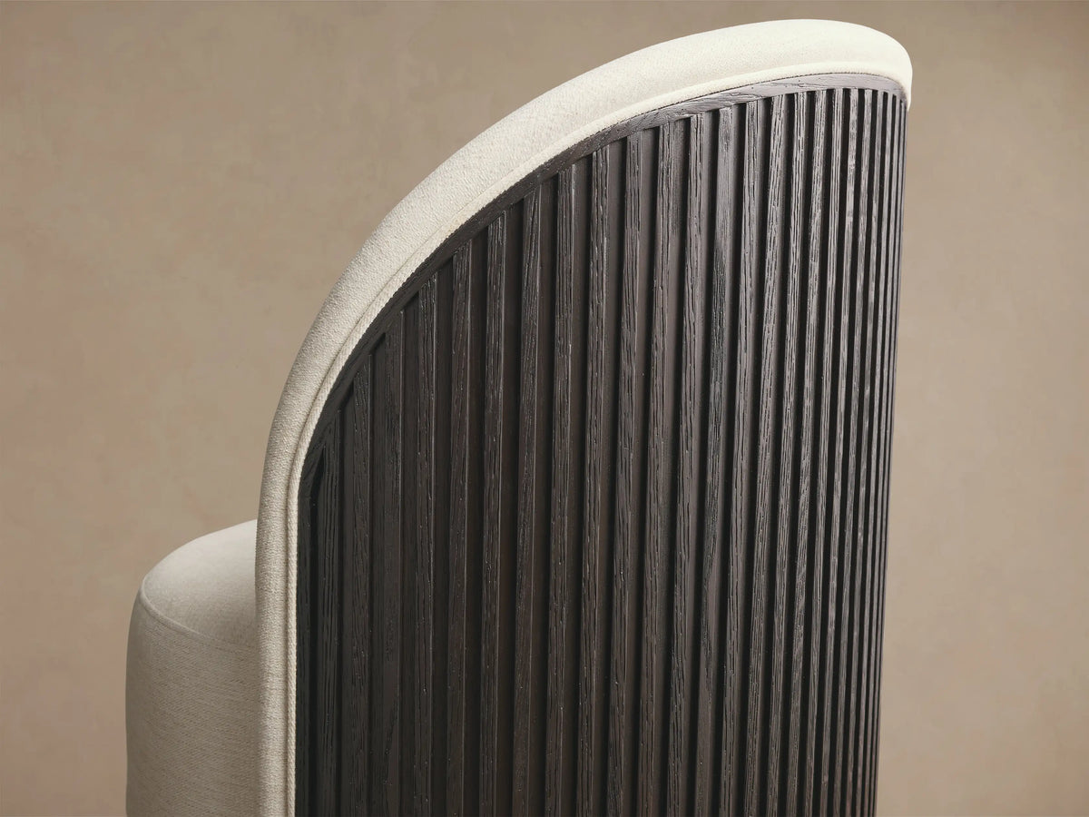 Side profile of the Finnley Dining Side Chair, with an off-white upholstered seat, Ebony reeded back, and brass plinth base.