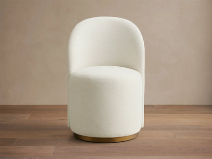 Front view of the off-white upholstered Finnley Dining Side Chair with a rounded back and brass plinth base.