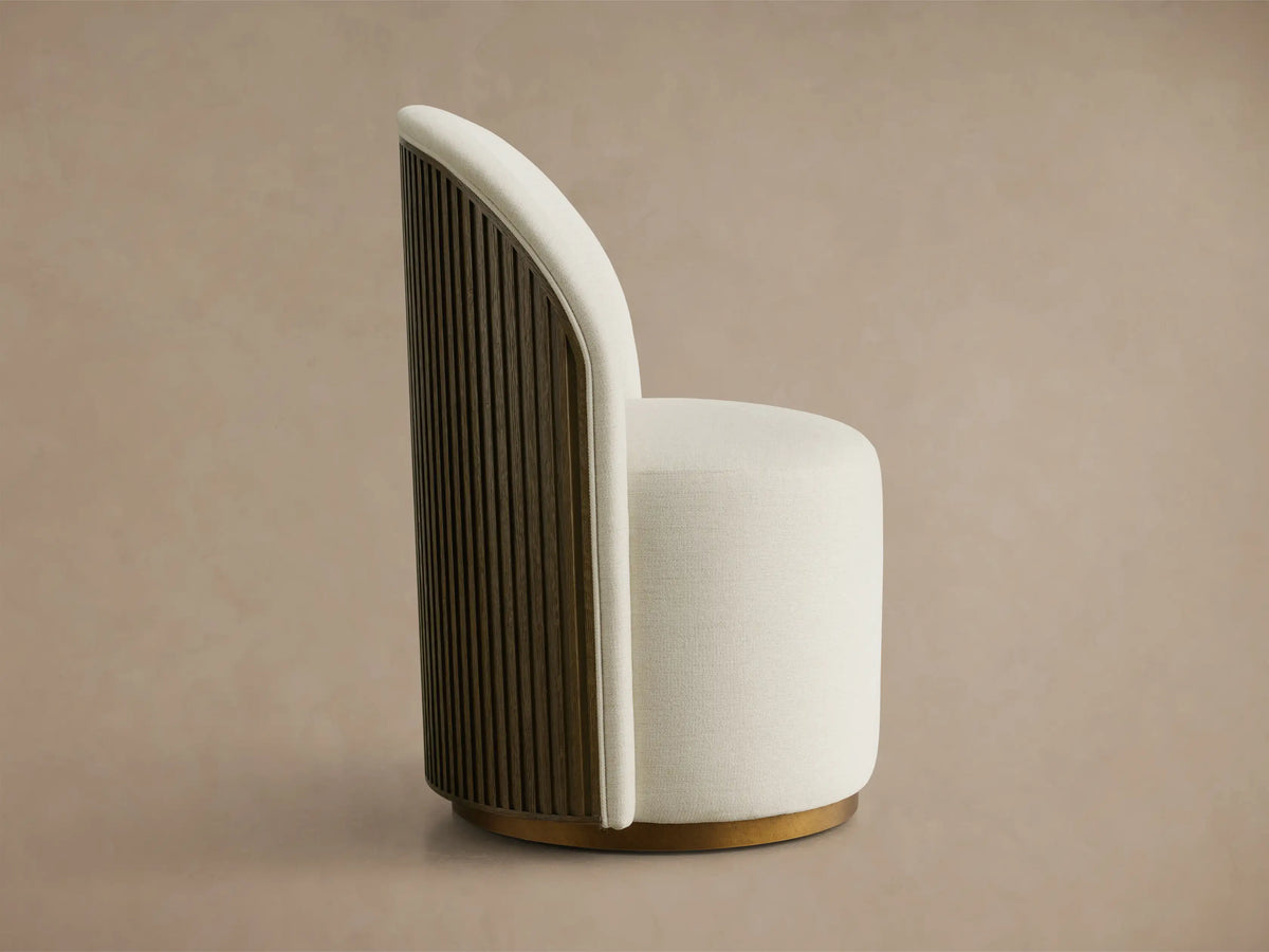 Side profile of a Finnley Dining Side Chair with cream upholstery, a curved Mocha reeded wood back, and a brass plinth base.