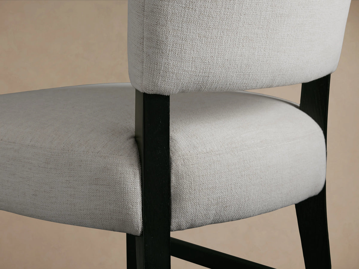 Fallyn Stool with a tall, upholstered white backrest and seat, black wooden legs with footrests, on a wooden floor against a beige wall.