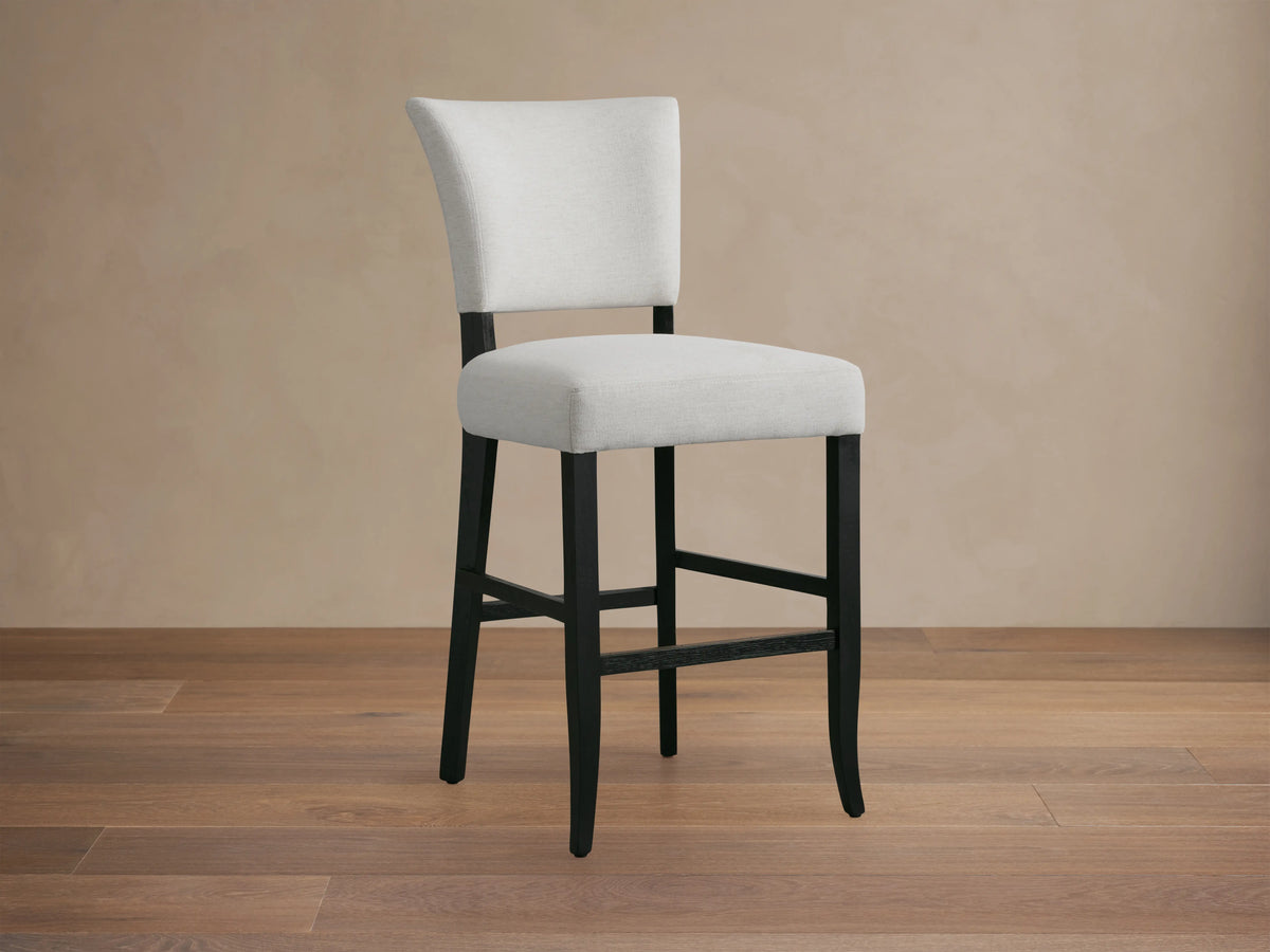 Fallyn Stool featuring a white cushioned seat and backrest with hand-painted black oak legs, shown from a side angle against a neutral background.