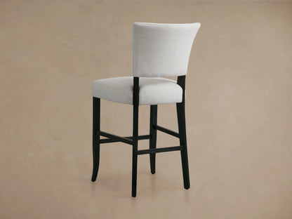 The Fallyn Stool features a light gray upholstered back and seat with dark wooden legs, set against a neutral background.