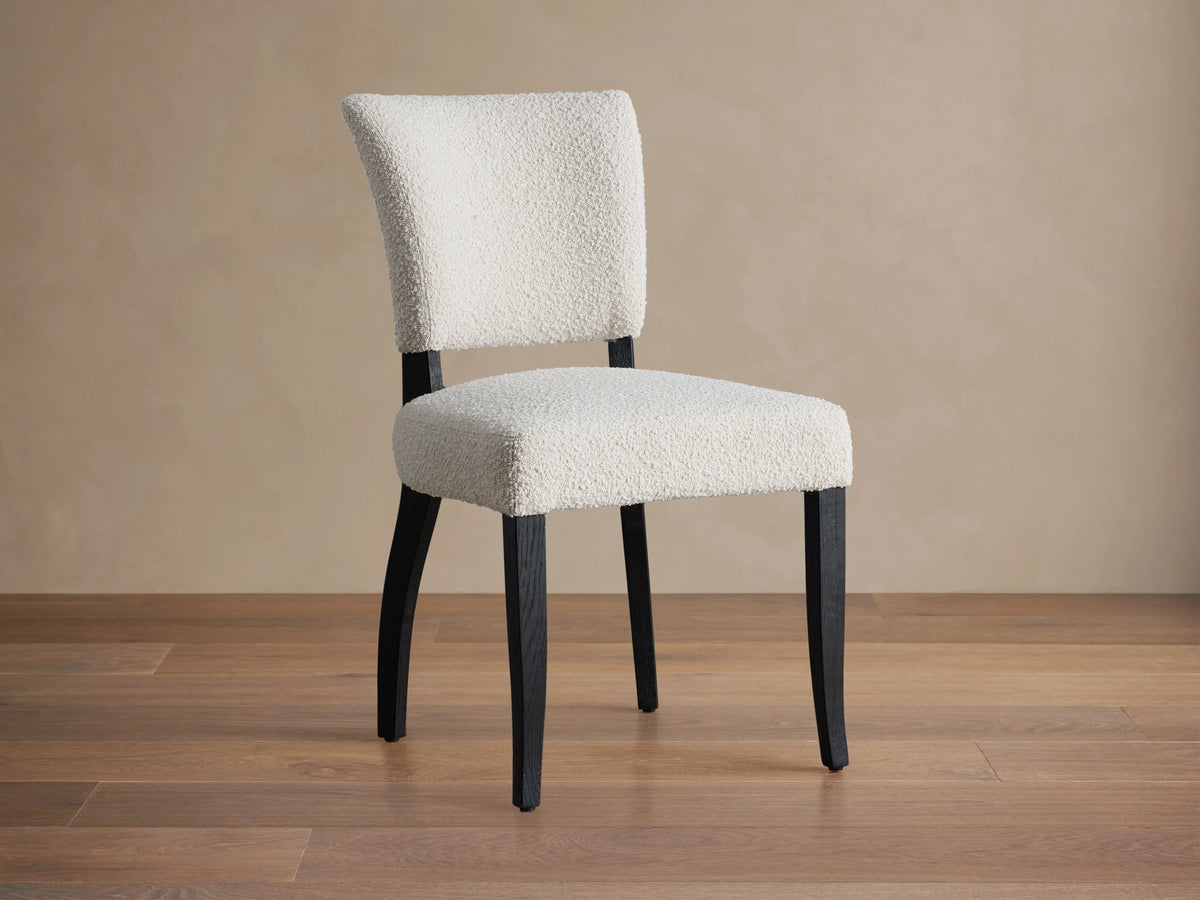 Fallyn Dining Side Chair with white, textured fabric upholstery, black solid wood legs, shown from a rear angled view on a beige background.