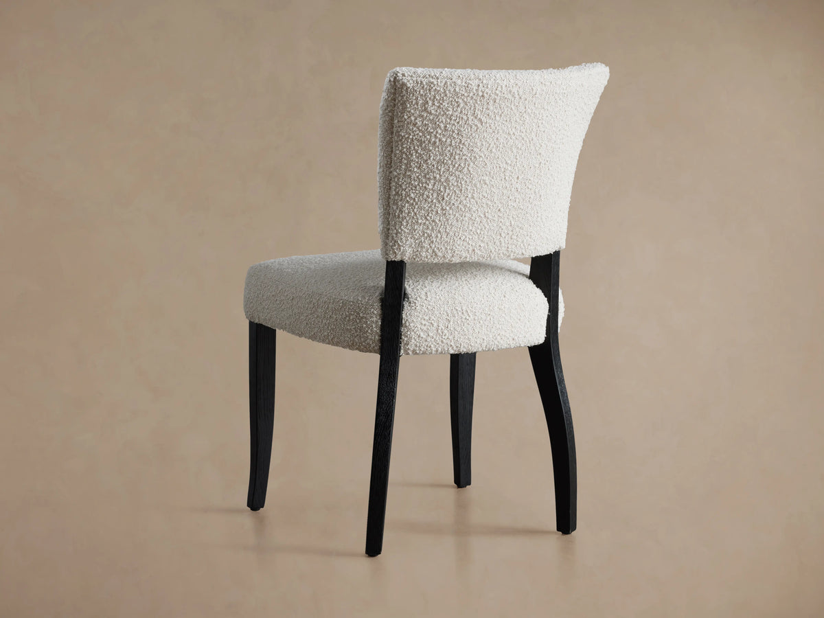 Fallyn Dining Side Chair with cream textured fabric upholstery, curved back, dark solid wood legs, on wooden floor.