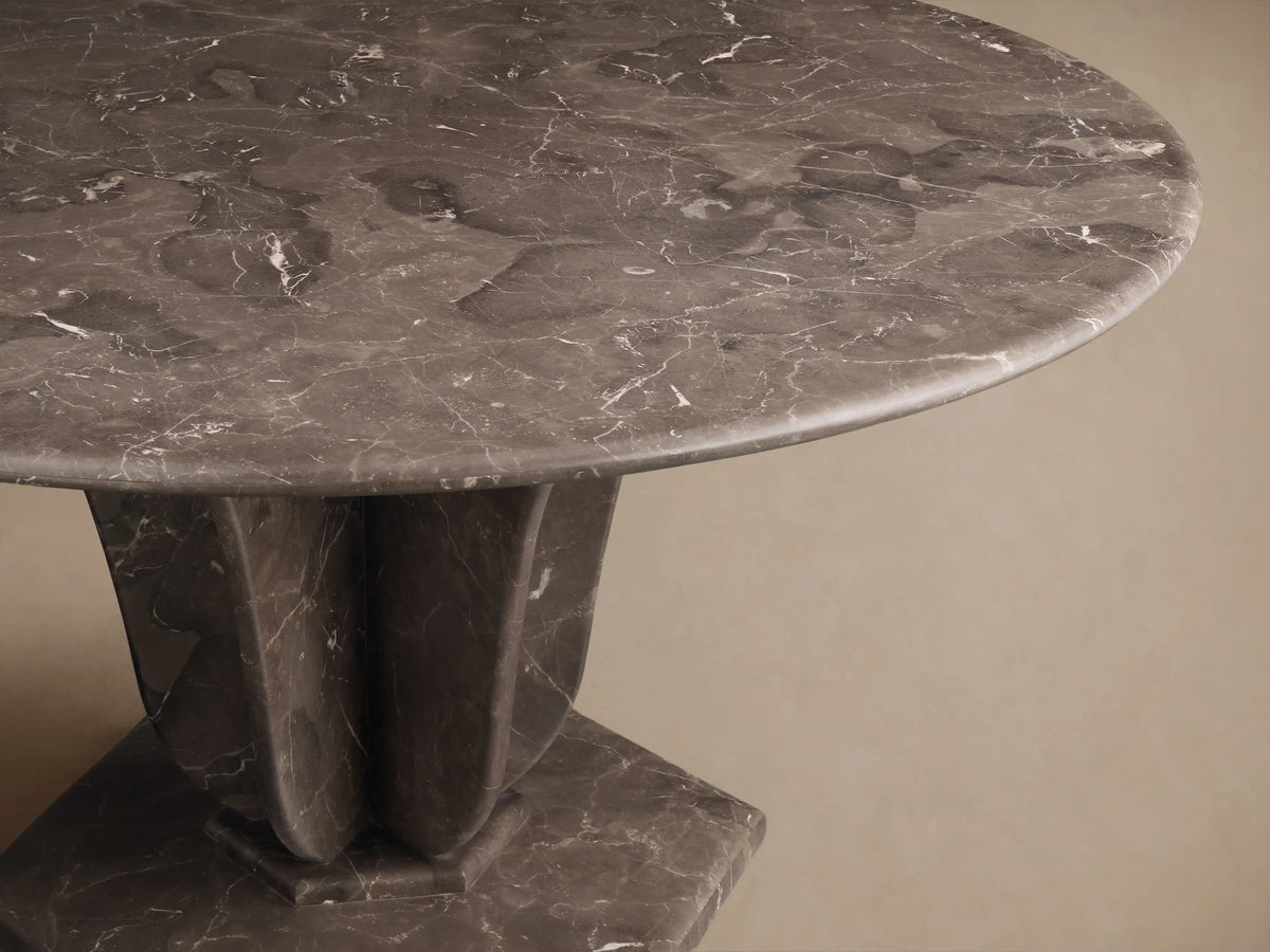 Angled view of the dark grey Gabriella Round Stone Dining Table with white veining and sculptural fin-style base.