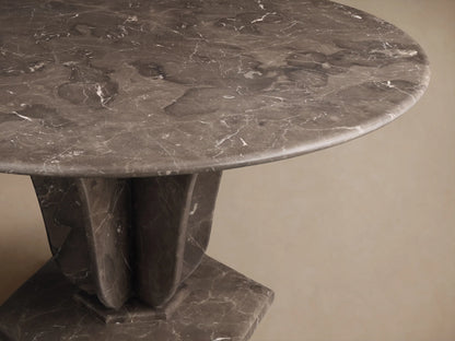 Angled view of the dark grey Gabriella Round Stone Dining Table with white veining and sculptural fin-style base.