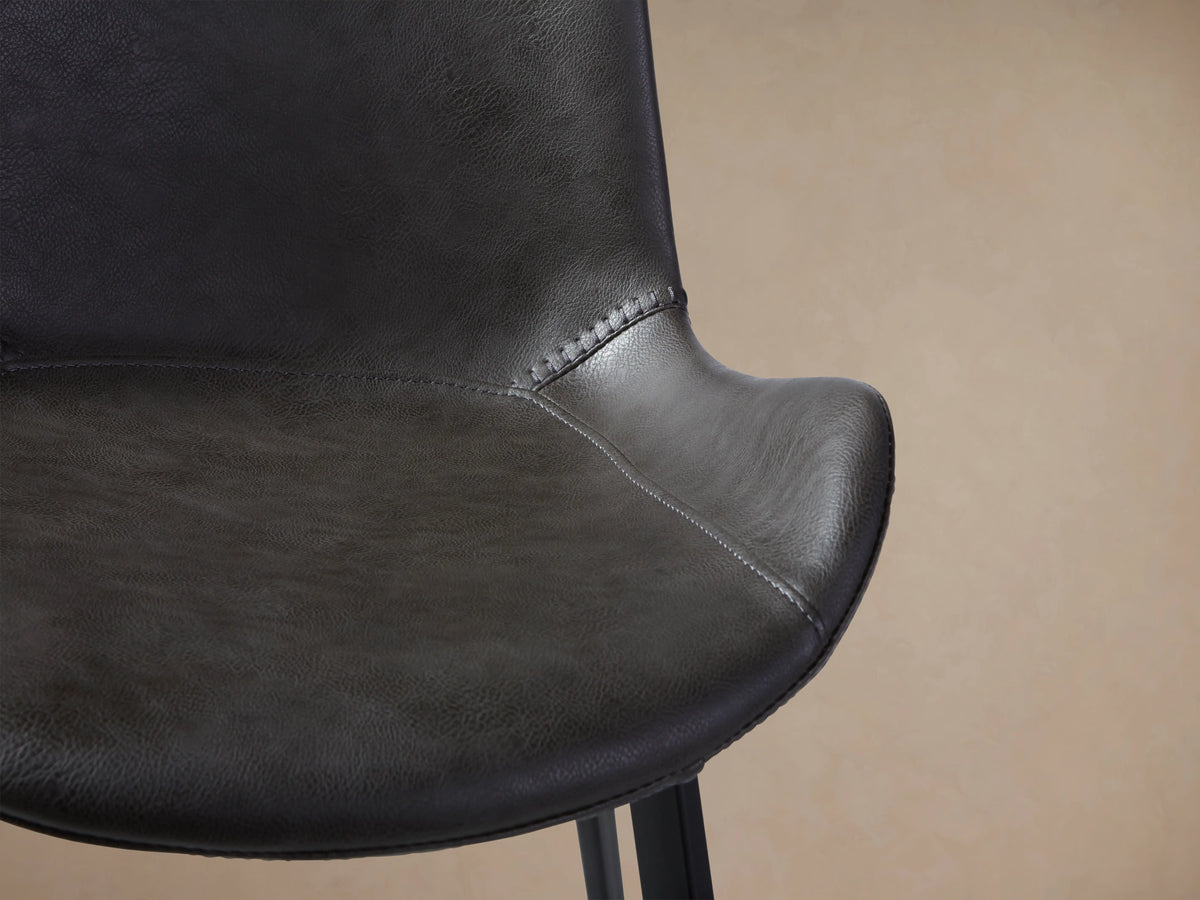 Gage Faux Leather Dining Chair: dark grey, front view, baseball stitching, black iron legs, on wood floor.