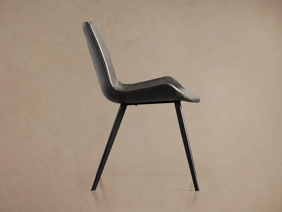 Gage Faux Leather Dining Chair, dark gray, viewed from back-right, showing curved back with stitching & black iron legs.
