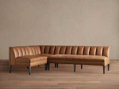 Gates L-shaped leather banquette in distressed caramel brown with channel-stitched backs, dark tapered legs, on wood floor.