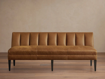 Gates Leather Settee, a tan leather bench with a channel-tufted backrest, smooth seat, and dark tapered legs, against a light wall.