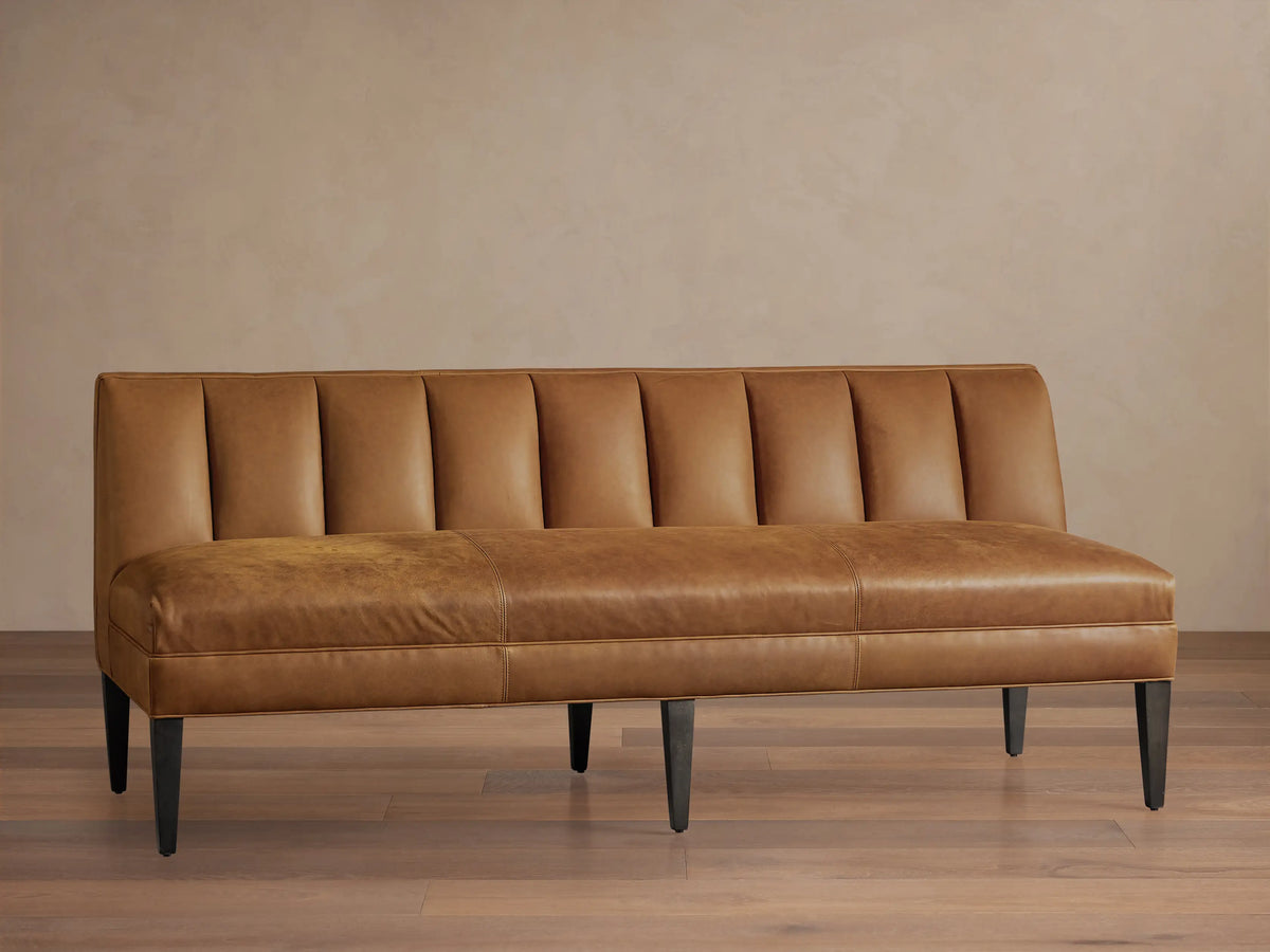 Gates Leather Settee, a tan leather bench with a channel-tufted backrest, smooth seat, and dark tapered legs, against a light wall.