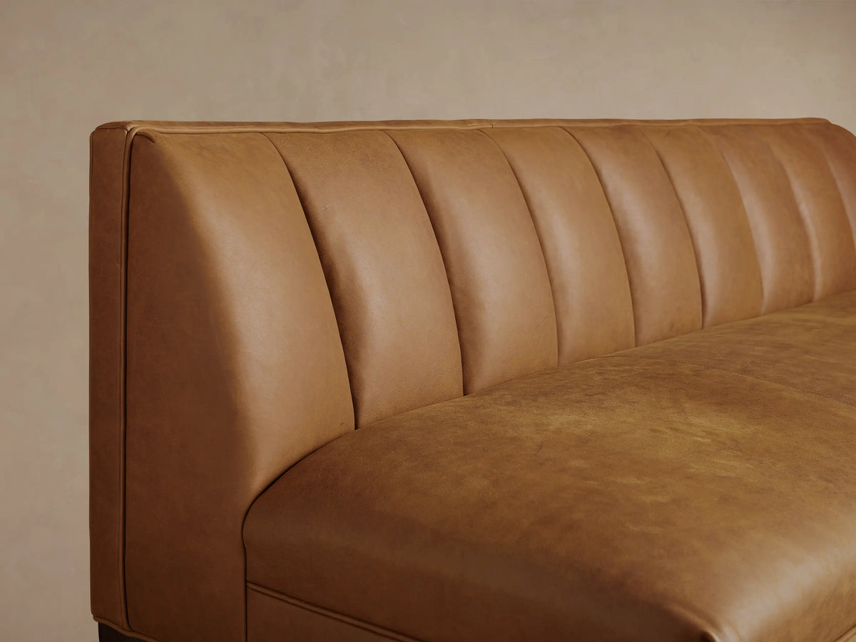 Gates Leather Settee: Distressed light brown leather settee with vertical channeled back, dark tapered legs, on wood floor.