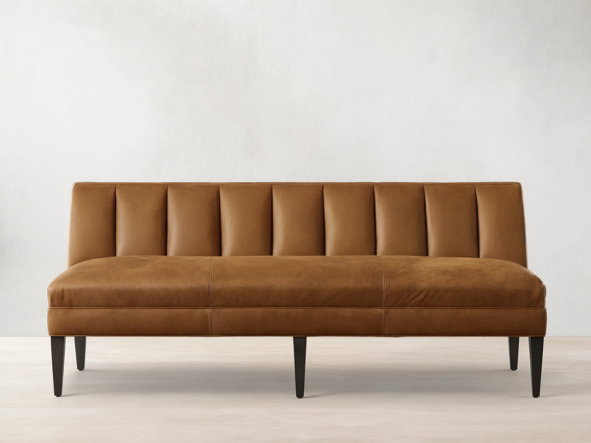 Gates Leather Settee, a tan leather bench with a channel-tufted backrest, smooth seat, and dark tapered legs, against a light wall.