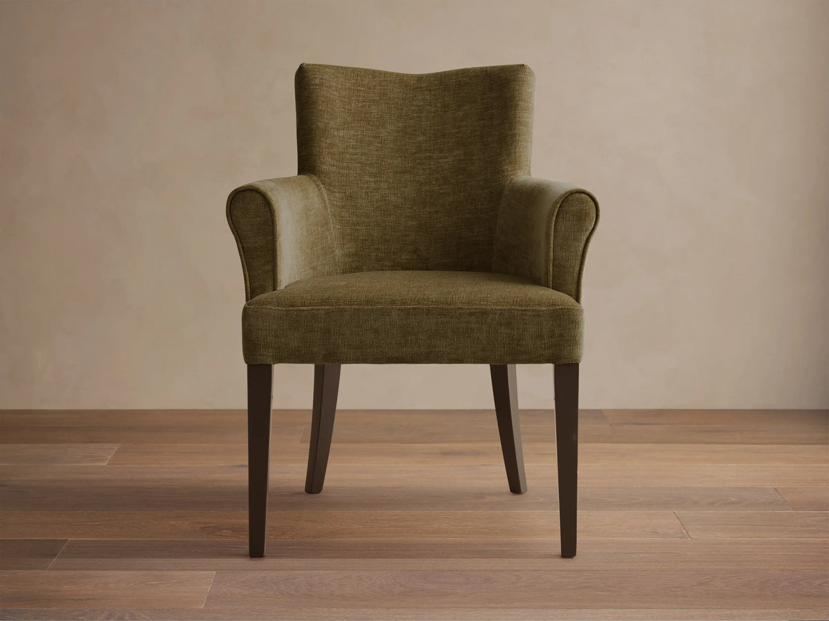 Front view of the olive green Giovanni Dining Arm Chair, featuring a textured upholstery, high back, rolled armrests, and dark wood legs.
