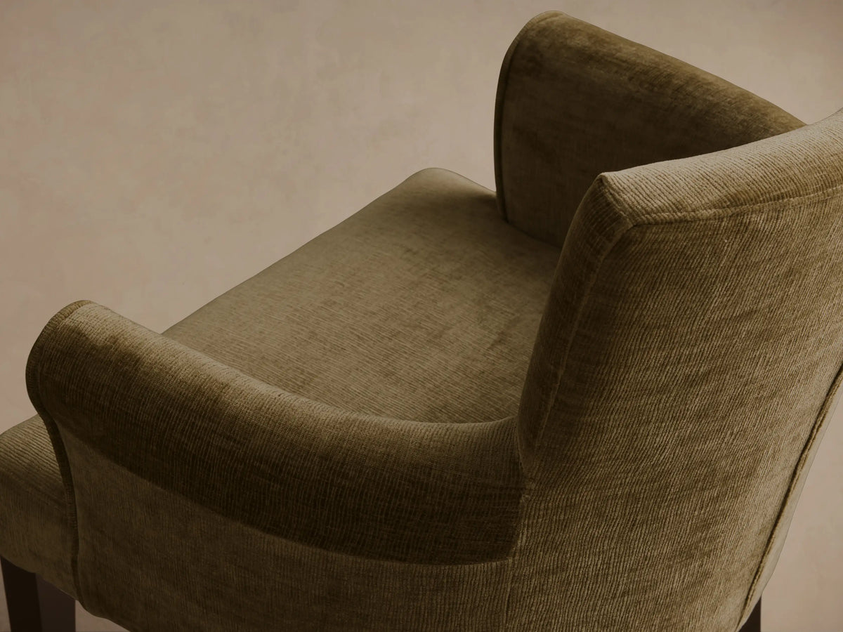 Close-up, angled view of the olive green ribbed Giovanni Dining Arm Chair, showing the padded back and curved armrest.