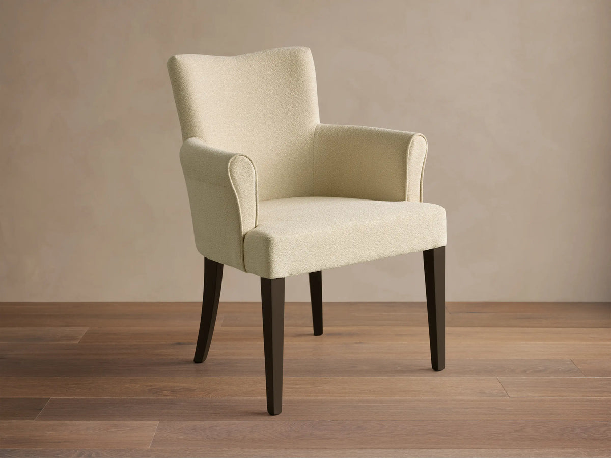 Front view of the cream upholstered Giovanni Dining Arm Chair with dark brown tapered wood legs.