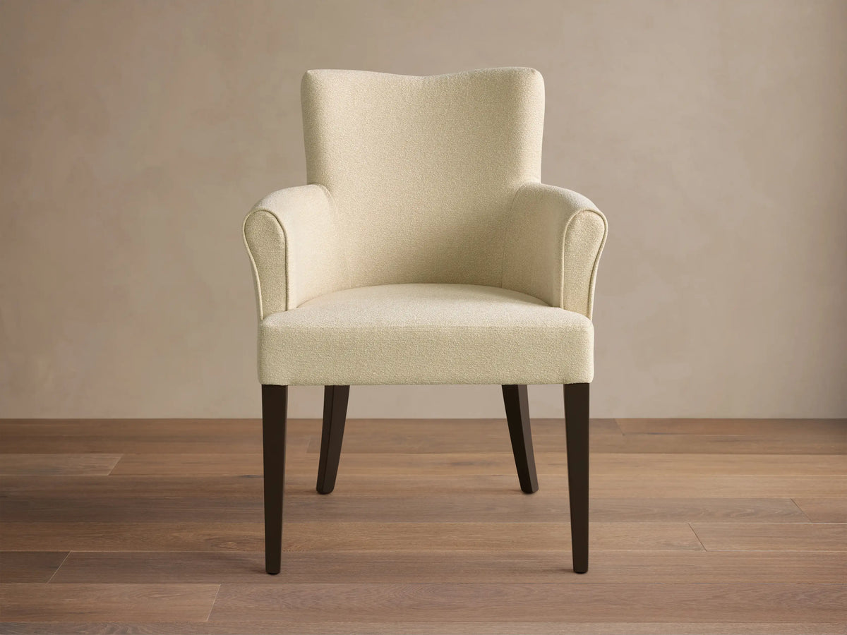 Front view of the cream textured Giovanni Dining Arm Chair with a gently curved backrest, armrests, and dark wood legs.