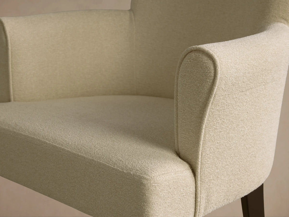 Close-up of the cream upholstered Giovanni Dining Arm Chair, showing the curved armrest and seat with textured fabric.