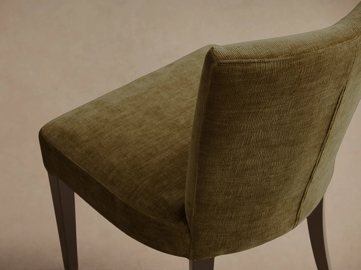 Rear view of a green textured upholstered Giovanni Dining Side Chair with a gently curved backrest and dark wooden legs.