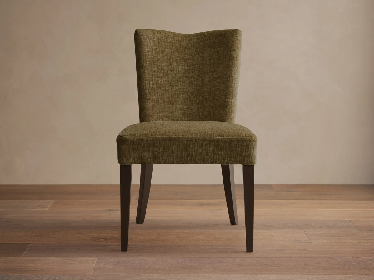 Close-up, angled view of the textured olive green Giovanni Dining Side Chair, showing the padded seat and backrest with dark wood legs.
