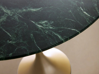 Saint Germain Bar Table with a round green marble top and sleek, gold-toned steel pedestal base, on a wooden floor.