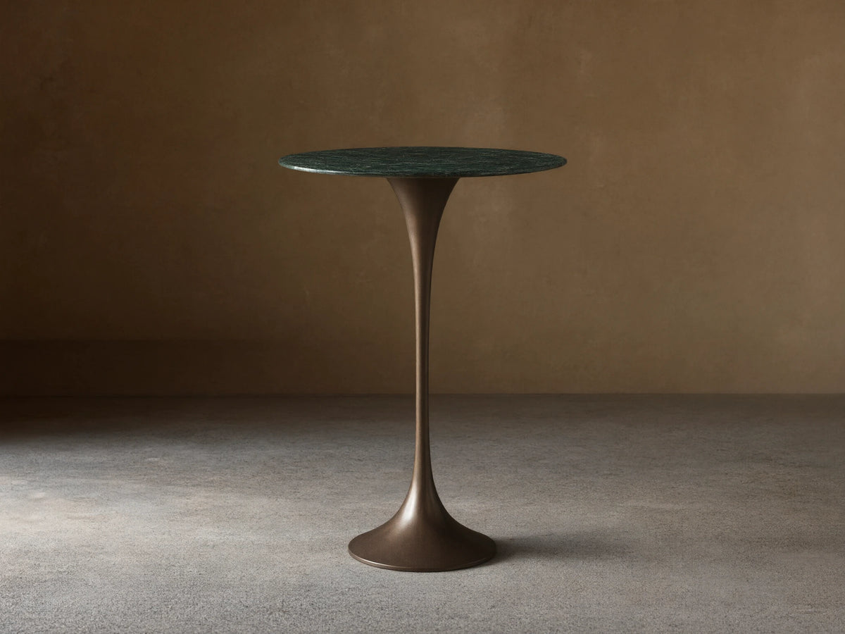 Front view of the Saint Germain Bar Table with a round dark green natural stone top and a dark bronze trumpet-shaped steel base.