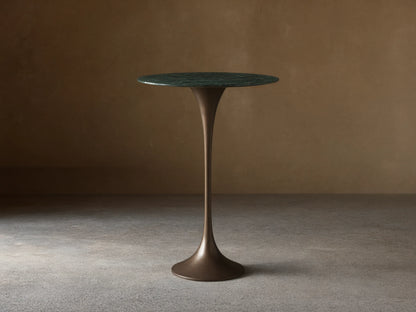 Front view of the Saint Germain Bar Table with a round dark green natural stone top and a dark bronze trumpet-shaped steel base.