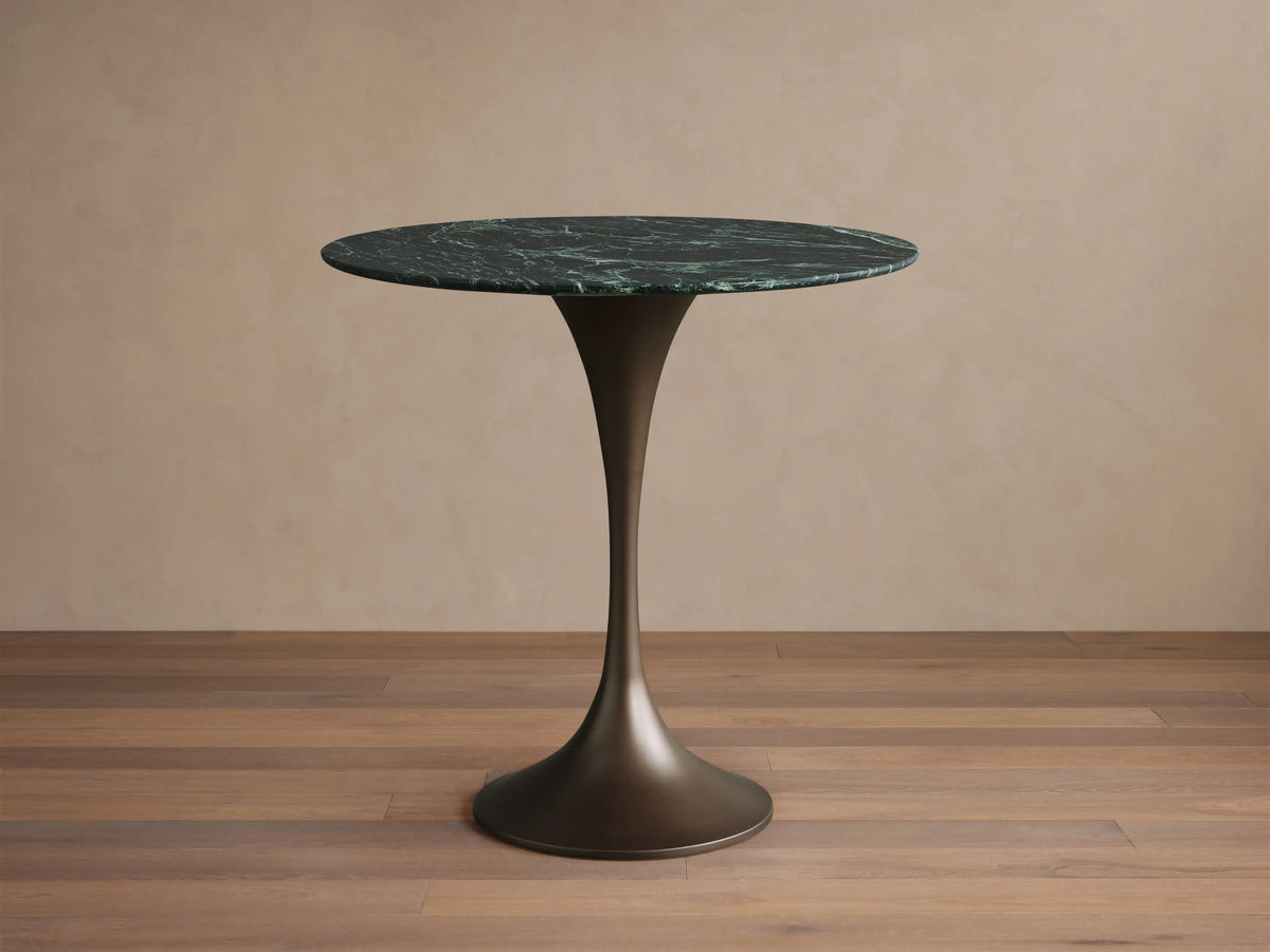 Round green marble tabletop with white veining, close-up view. Tabletop rests on a steel base with a smooth, elegant finish.