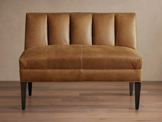 Gates Leather Bench, tan brown, front view. Channel-stitched back, flat seat, dark tapered legs on wood floor.