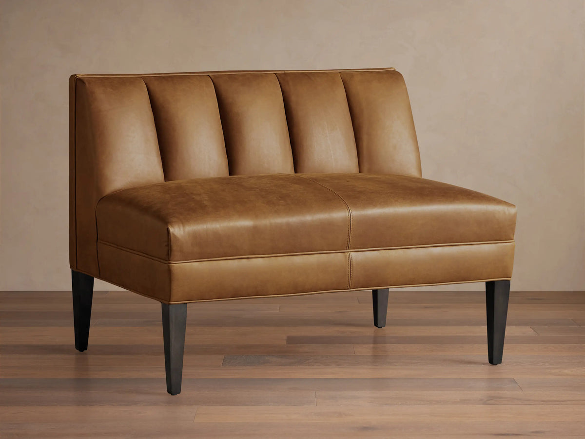 Gates Leather Bench, tan brown, front view. Channel-stitched back, flat seat, dark tapered legs on wood floor.