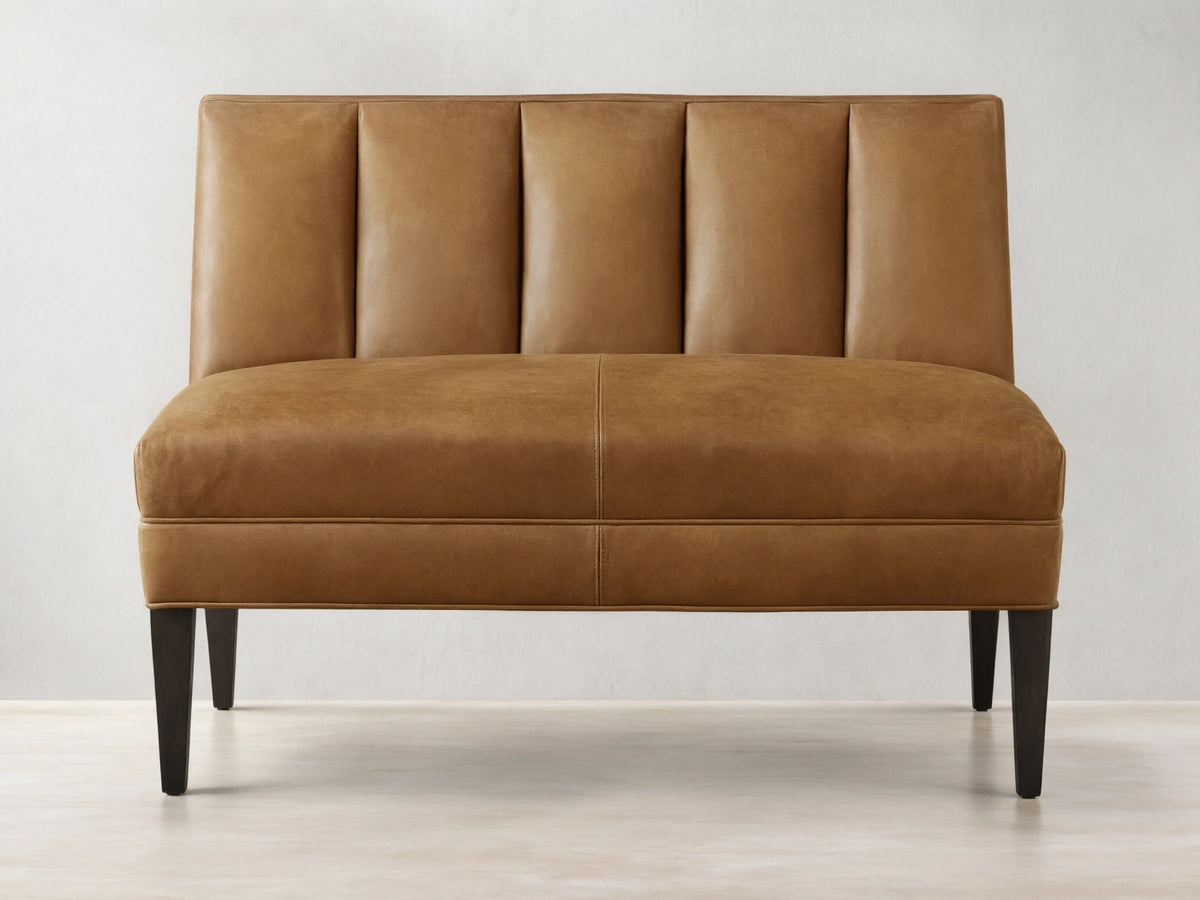 Gates Leather Bench, tan brown, front view. Channel-stitched back, flat seat, dark tapered legs on wood floor.