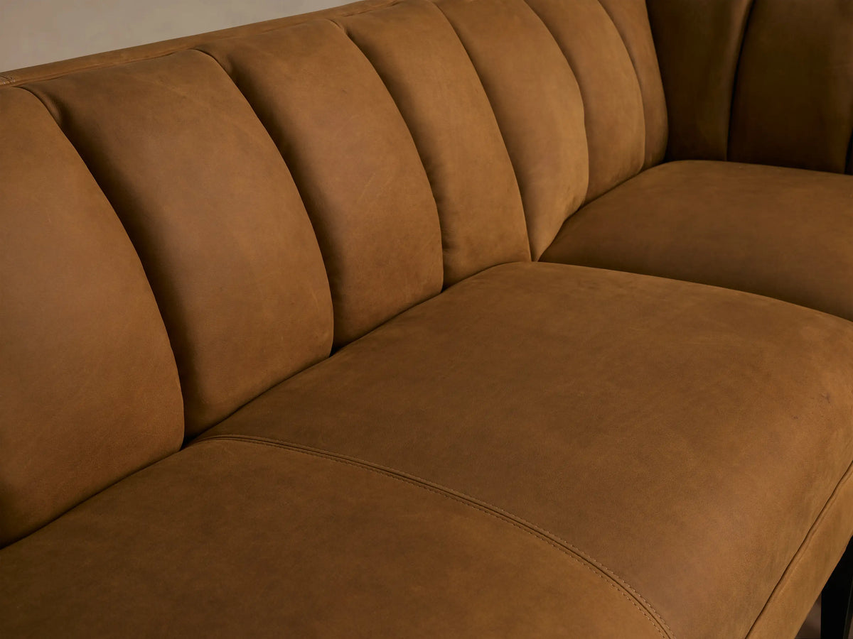 Gates U-shaped banquette in rich brown leather, channel-stitched back, dark tapered legs, on a light wood floor.