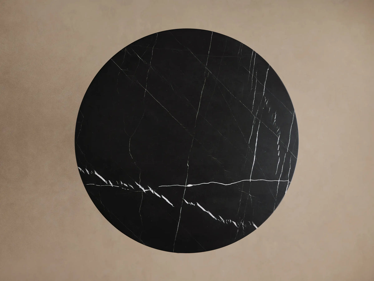 Hemmings Bistro Table, close-up of its round black marble top & cylindrical base with striking white veining on a light background.