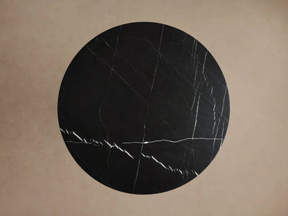 Hemmings Bistro Table, close-up of its round black marble top & cylindrical base with striking white veining on a light background.