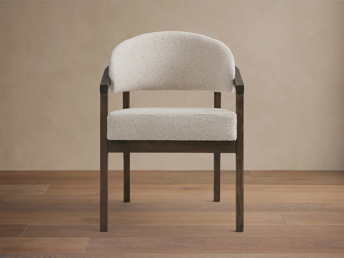 Front view of the Hagen Dining Chair featuring a padded cream seat and backrest, with curved arms and a dark wooden frame.