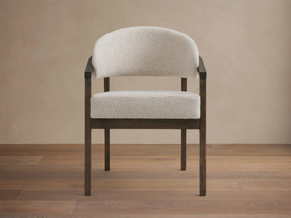 Front view of the Hagen Dining Chair featuring a padded cream seat and backrest, with curved arms and a dark wooden frame.